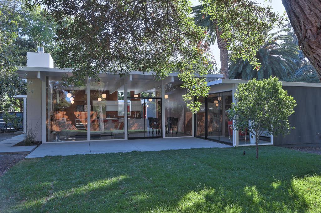 Exterior view of Eichler home with glass walls and dining area visible through trees